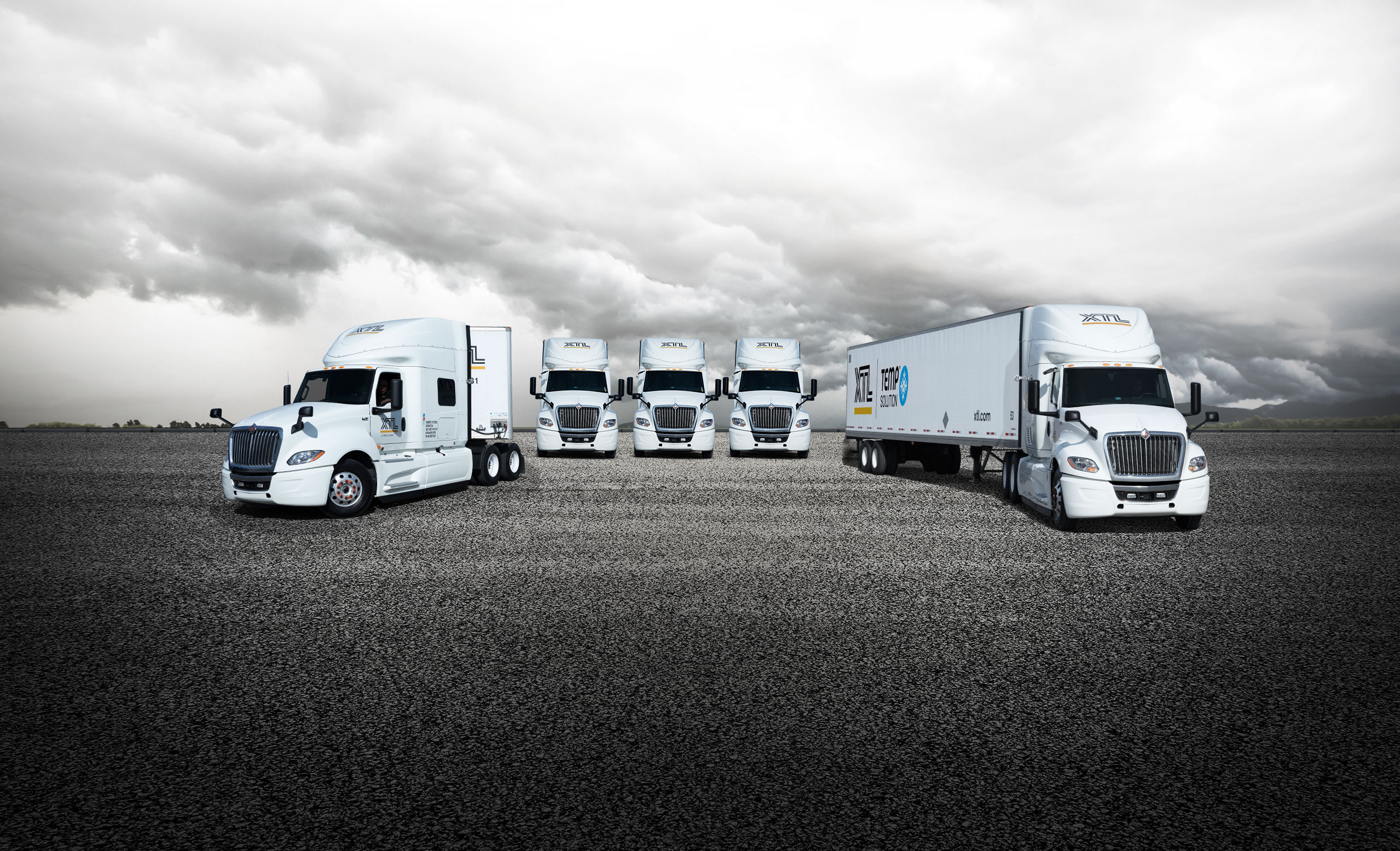 Cinq camions XTL stationnés dans une cour asphaltée